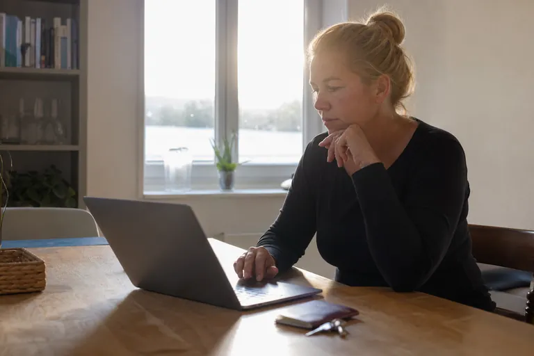 Vermieterin bearbeitet am Laptop den Anreiseablauf neben Reisepass und Schlüsseln